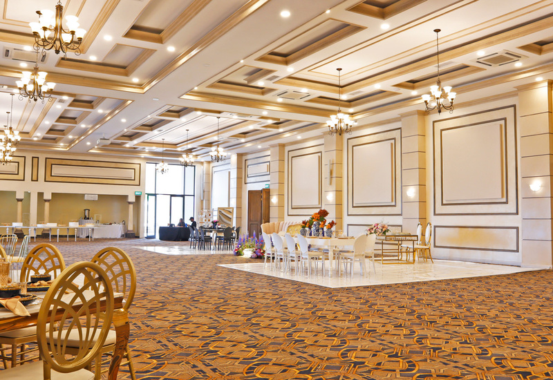 Grand hotel ballroom with coffered ceiling, chandeliers, patterned carpet, set dining tables and floral centerpieces.