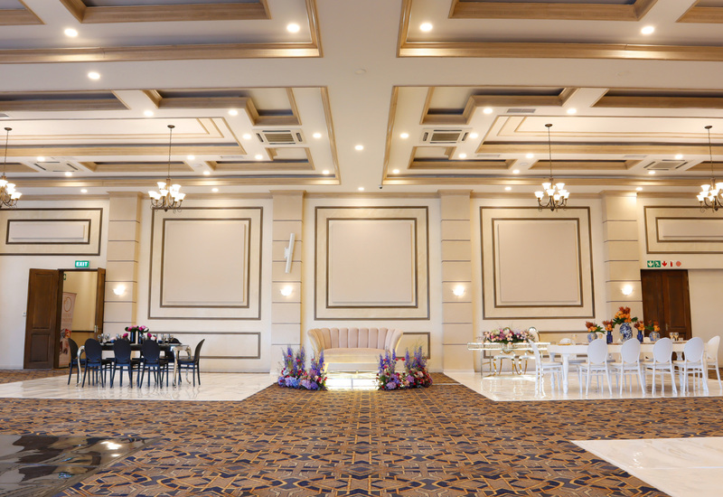 Elegant hotel ballroom with coffered ceiling and chandeliers, velvet settee, dining tables and floral arrangements.