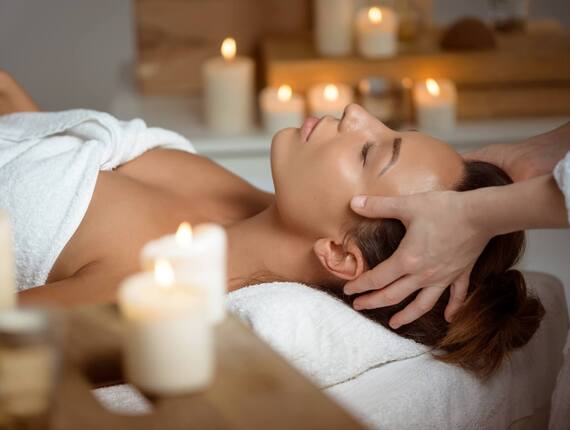 Relaxing spa scene: guest receiving a soothing head and neck massage on white towels amid lit candles.