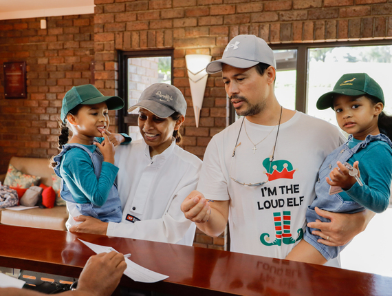 Family checking in at reception — parents holding two young children in a warm brick-walled lobby with sofa as staff hands over keys.