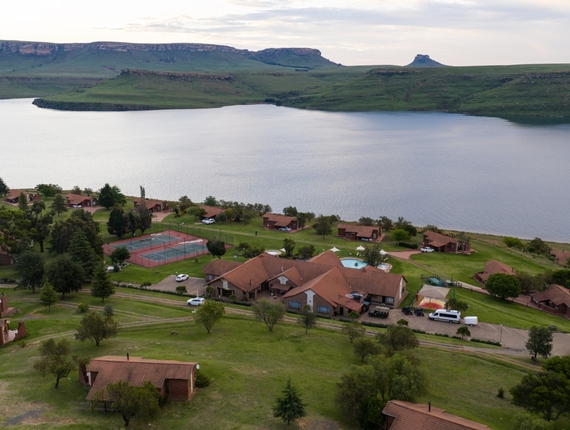 Qwantani red-tiled cottages, pool, tennis courts and green lawns overlooking a calm lake and rolling hills.