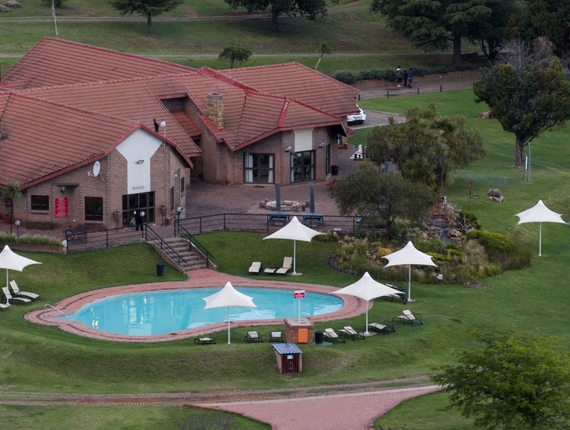 Qwantani with red tile roofs overlooking a kidney-shaped pool, white parasols, lounge chairs and a rock waterfall garden.