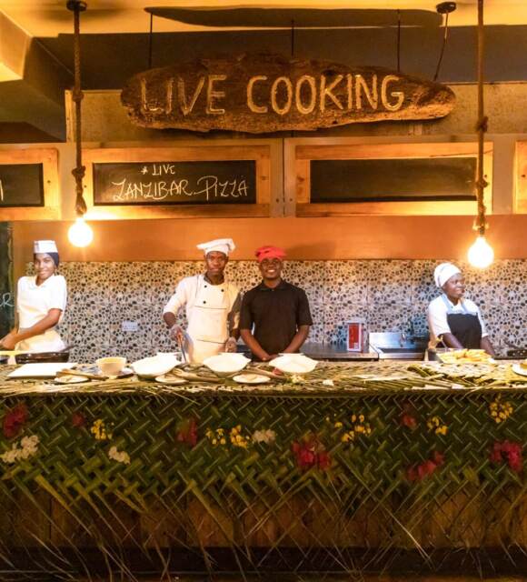 Chefs prepare live cooking dishes including kachori, Zanzibar pizza, and beef samosa at a vibrant hotel food station