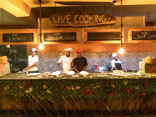 Chefs prepare live cooking dishes including kachori, Zanzibar pizza, and beef samosa at a vibrant hotel food station