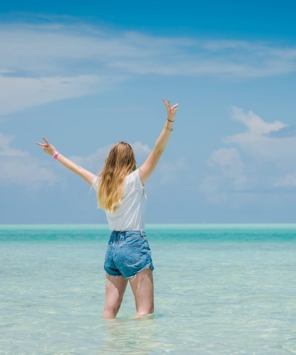 Guest enjoying shallow, clear turquoise ocean water under a bright blue sky, celebrating a beach vacation moment