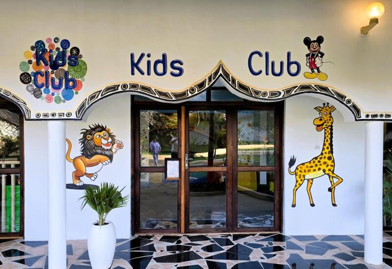 Colorful Kids Club entrance with fun animal murals, wooden double doors, decorative arches, and tiled floor at family-friendly hotel