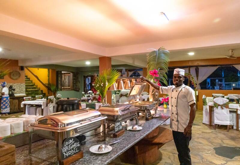 Chef serving warm local vegetable noodles and brown beef stew at an indoor buffet with decorated dining tables
