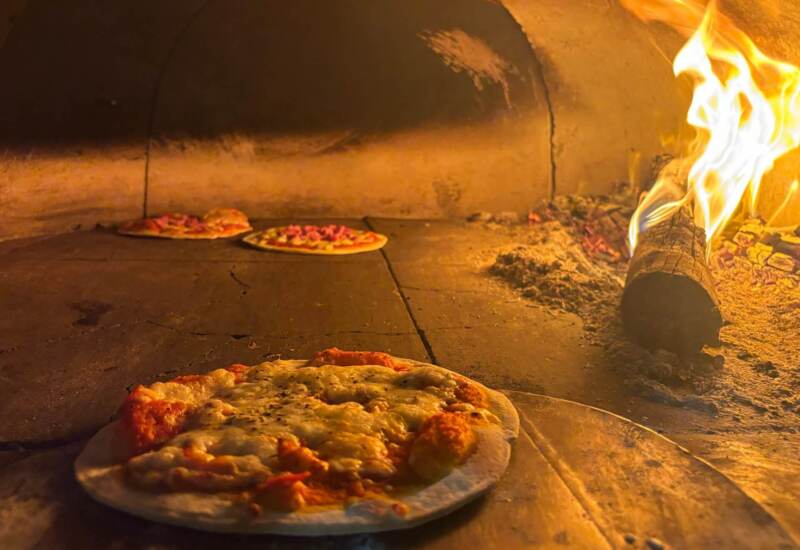 Wood-fired pizzas baking inside a rustic stone oven with glowing flames and embers adding warmth and aroma