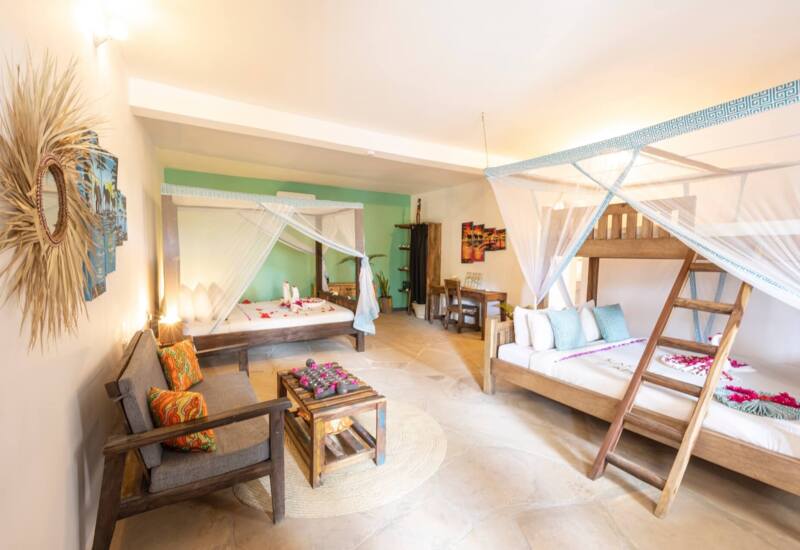 Spacious hotel suite with wooden four-poster and bunk beds, mosquito nets, cozy seating area, and tropical decor accents