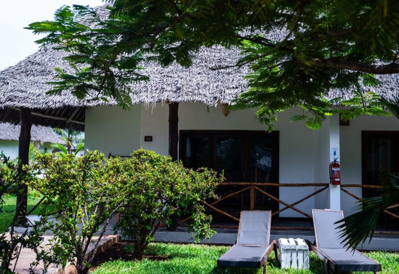Tropical thatched-roof bungalow with wooden railings, private patio, and lounge chairs set in lush greenery