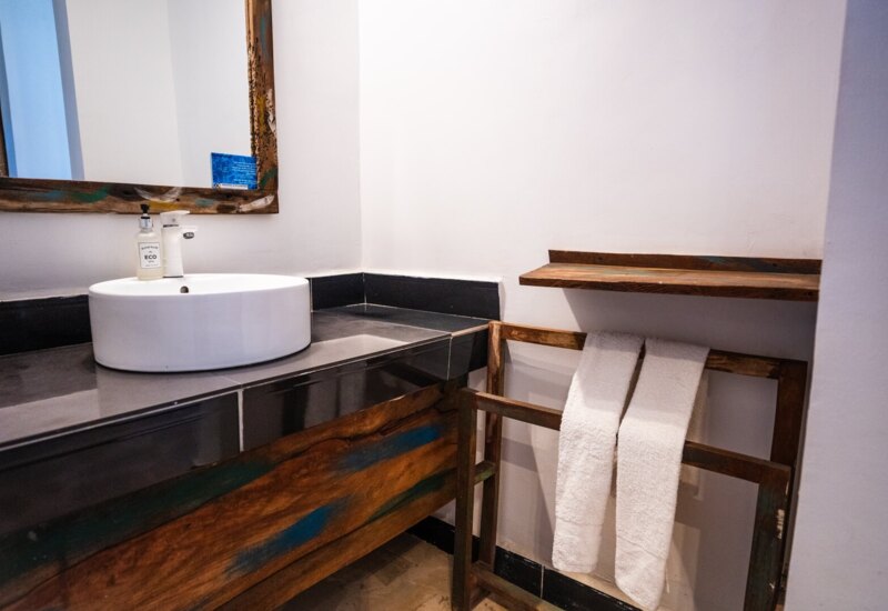 Bathroom with round white sink on black countertop, rustic wooden mirror and towel rack holding two white towels