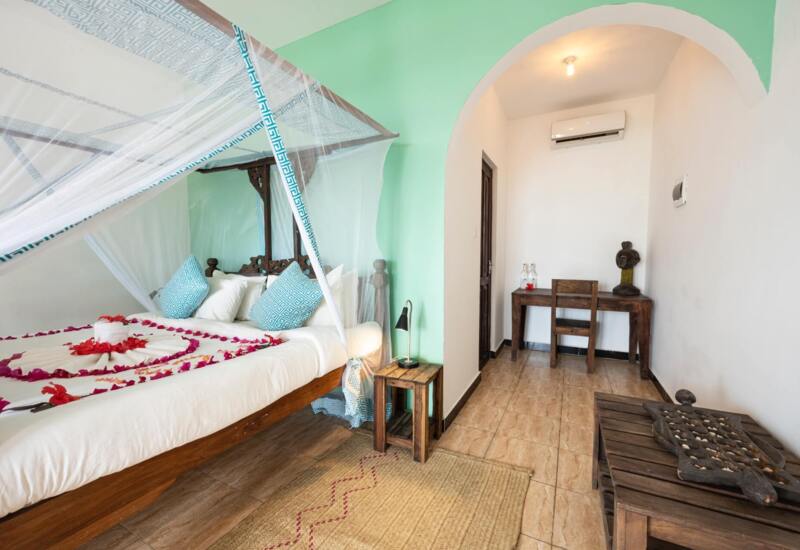 Cozy hotel room with a wooden four-poster bed draped in white mosquito netting and pillows, decorated with flower petals.