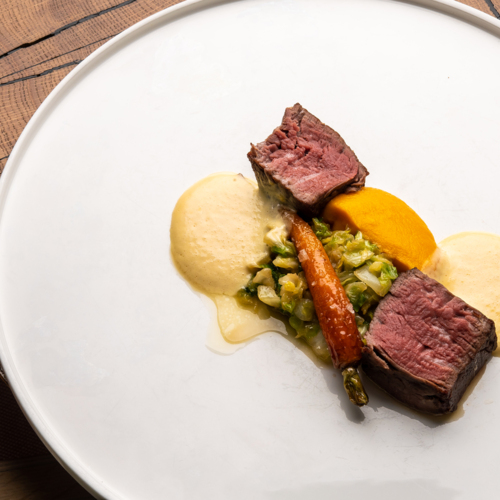 Minimalistyczne danie z mięsem i warzywami na białym talerzu.