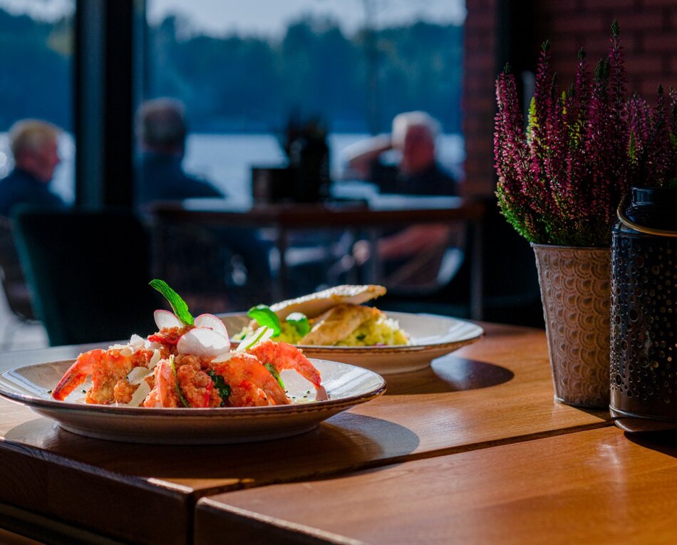 Krewetki z dodatkami na talerzu w restauracji z widokiem na wodę, w tle goście przy stole, rustykalna atmosfera