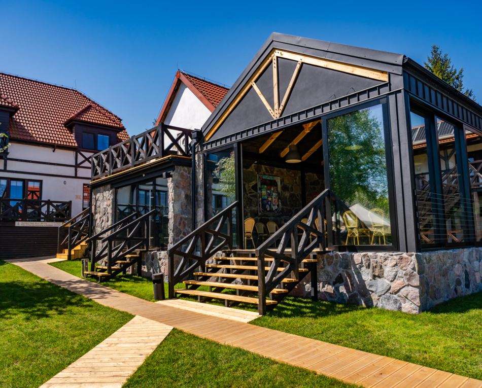 Hotel o tradycyjnym i nowoczesnym stylu z kamienną elewacją, dużymi szklanymi oknami i tarasem na trawie