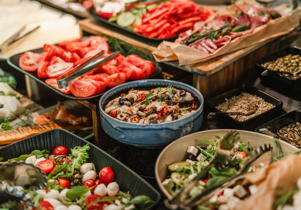 Bufet hotelowy z sałatkami: świeże plastry pomidorów, mieszane sałaty, antipasti, oliwki, pestki i szczypce