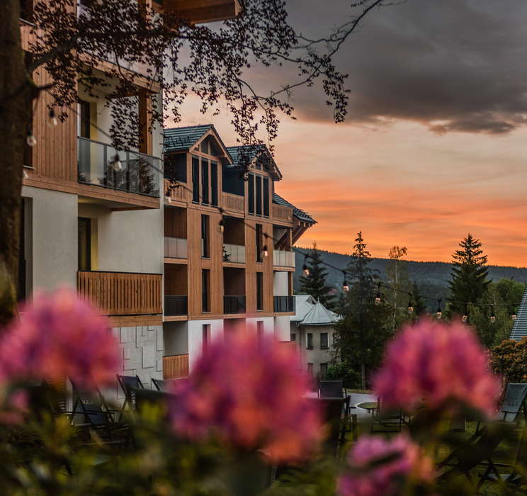 Górski hotel w stylu chalet z drewnianymi balkonami, ogrodowym miejscem do siedzenia i różowymi kwiatami na pierwszym planie
