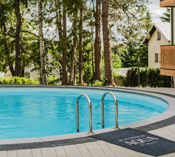 Outdoor hotel pool with stainless ladder, blue water, forested terrace view and modern wooden balconies nearby