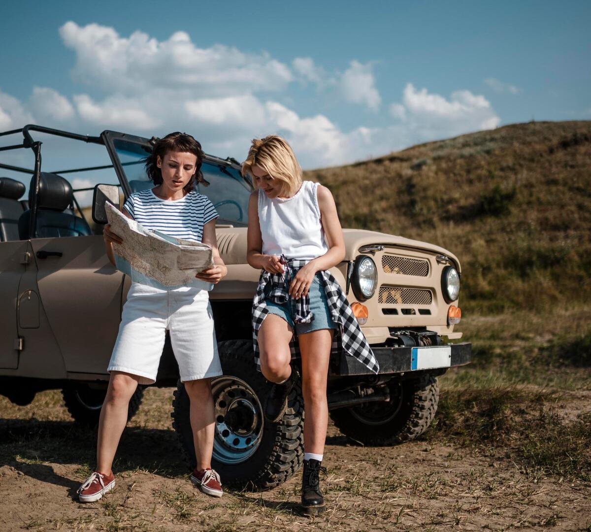 Zwei Reisende lehnen an einem beigen Geländewagen 4x4 und studieren eine Karte bei einer sonnigen Rast auf dem Land