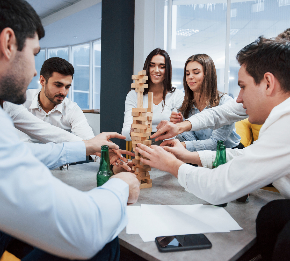 Junge Berufstätige spielen Jenga an einem Tisch in einer hellen Hotel-Meeting-Lounge während einer Teambuilding-Pause