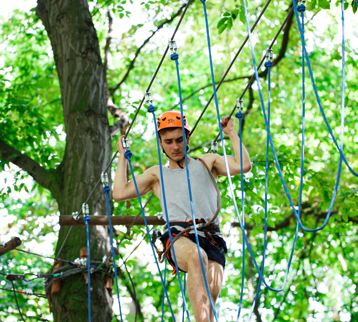 Gast auf Hochseilgarten im Wald, mit Klettergurt und orangefarbenem Helm