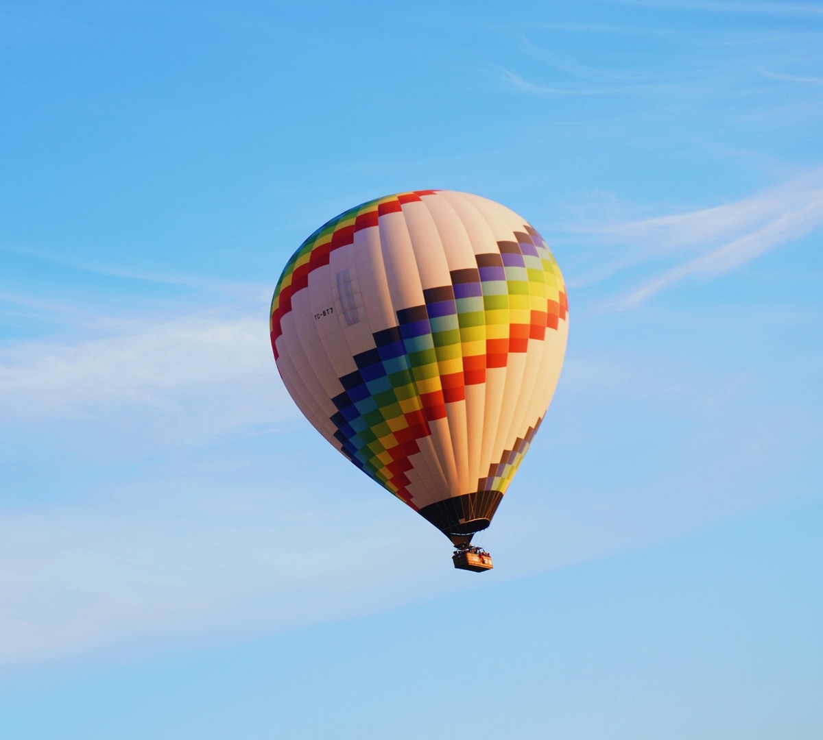 Bunter kariert gemusterter Heißluftballon steigt vor klarem blauem Himmel auf, Passagiere im Korb