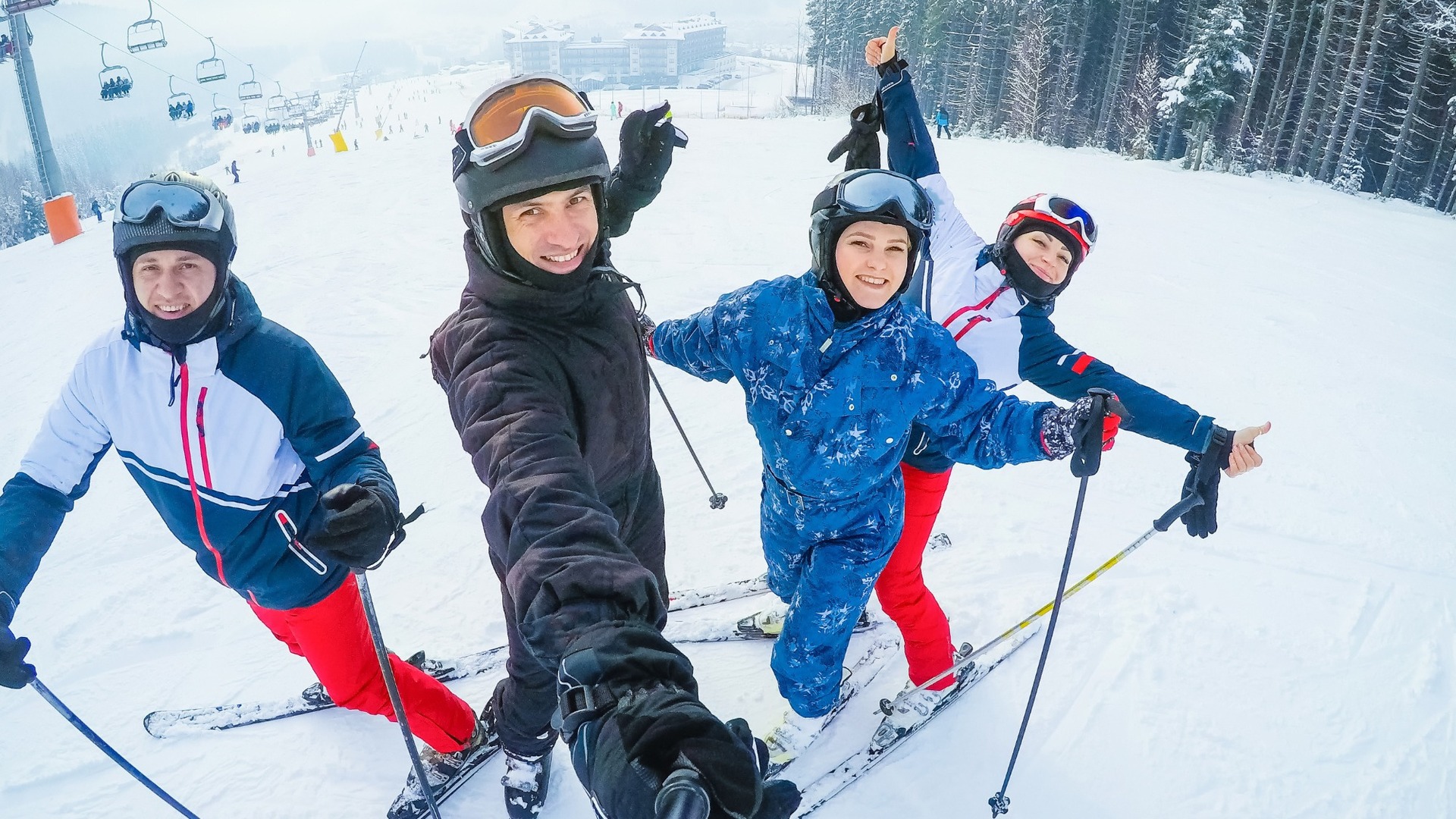 Gruppe lächelnder Skifahrer macht Selfie auf verschneiter Piste, Sessellift darüber und Hotel im Hintergrund