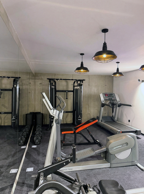 Small hotel gym with treadmill, elliptical, adjustable bench, dumbbell rack, mirrored wall and warm pendant lighting.