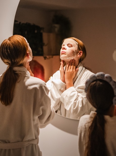 Gjester i hvite badekåper påfører arkmasker foran spa-speilet, avslappende ansiktsbehandling