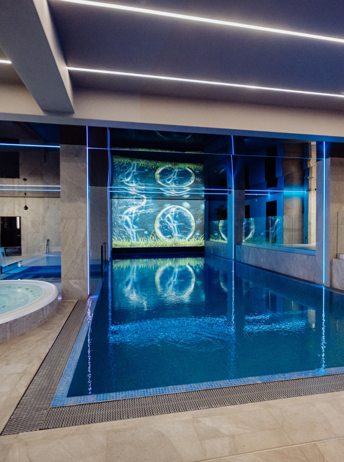 Wnętrze spa z podgrzewanym jacuzzi, basenem do pływania, leżakami i niebieskim oświetleniem LED