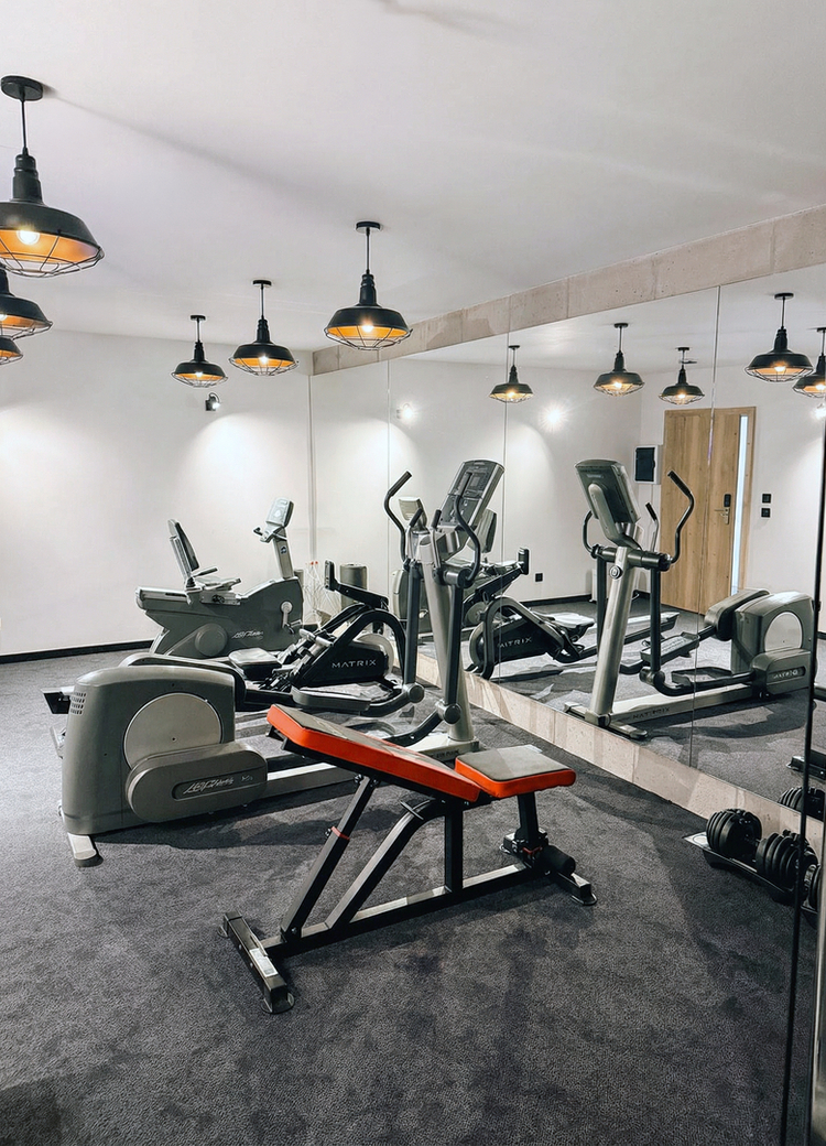 Hotel gym with treadmill, elliptical, adjustable bench, free weights and mirrored wall under warm pendant lights
