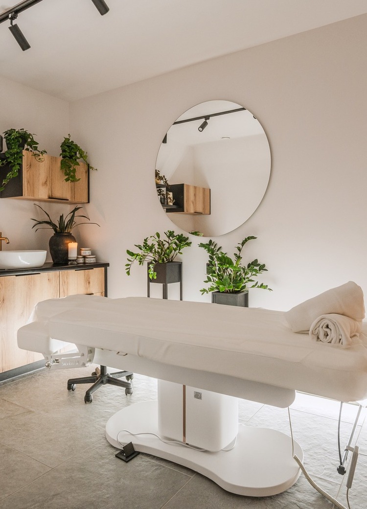 Spa treatment room with white massage table, rolled towels, candles, Himalayan salt lamp, wooden cabinets and plants