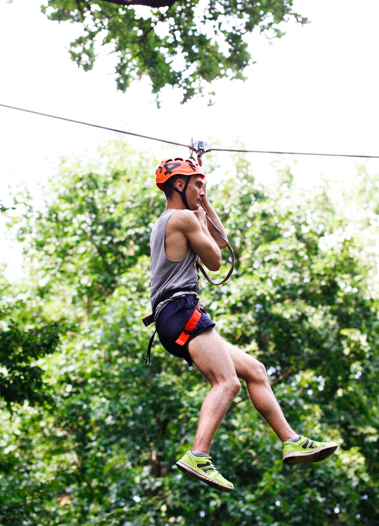 Gast mit Helm und Gurt gleitet an einer Zipline über grünem Blätterdach, Outdoor-Abenteuer.