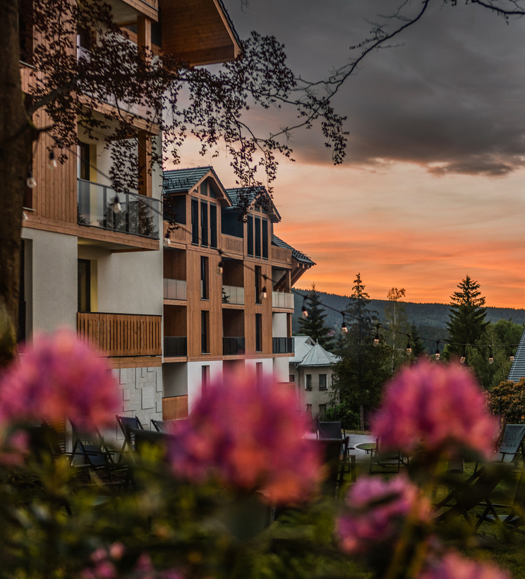 Chalet-style hotel with wooden balconies, garden seating and pink flowers in foreground at a mountain sunset