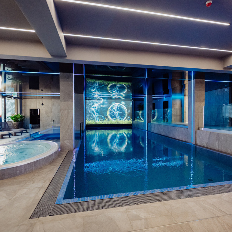 Vnitřní spa s vyhřívanou vířivkou, plaveckým bazénem, lehátky a modrým LED osvětlením