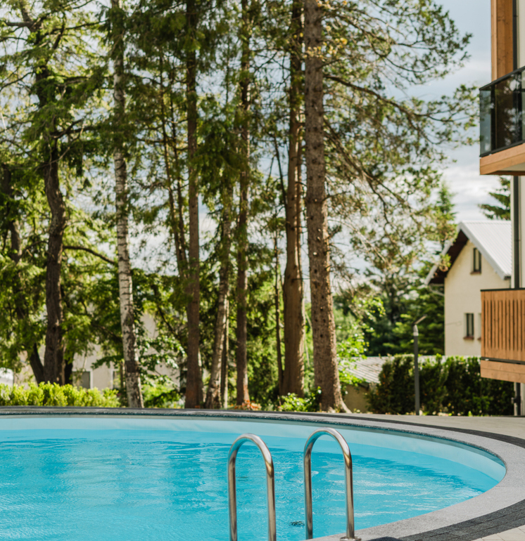 Outdoor hotel pool with stainless ladder, blue water, forested terrace view and modern wooden balconies nearby