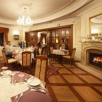 Elegancka restauracja hotelowa z kominkiem i kryształowym żyrandolem, mozaikową drewnianą podłogą, nakrytymi stołami i gośćmi.