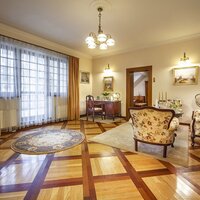 Klasyczny salon hotelowy z kwiatowymi fotelami, mozaikową podłogą, biurkiem, telewizorem, dużym oknem i przytulnym oświetleniem.