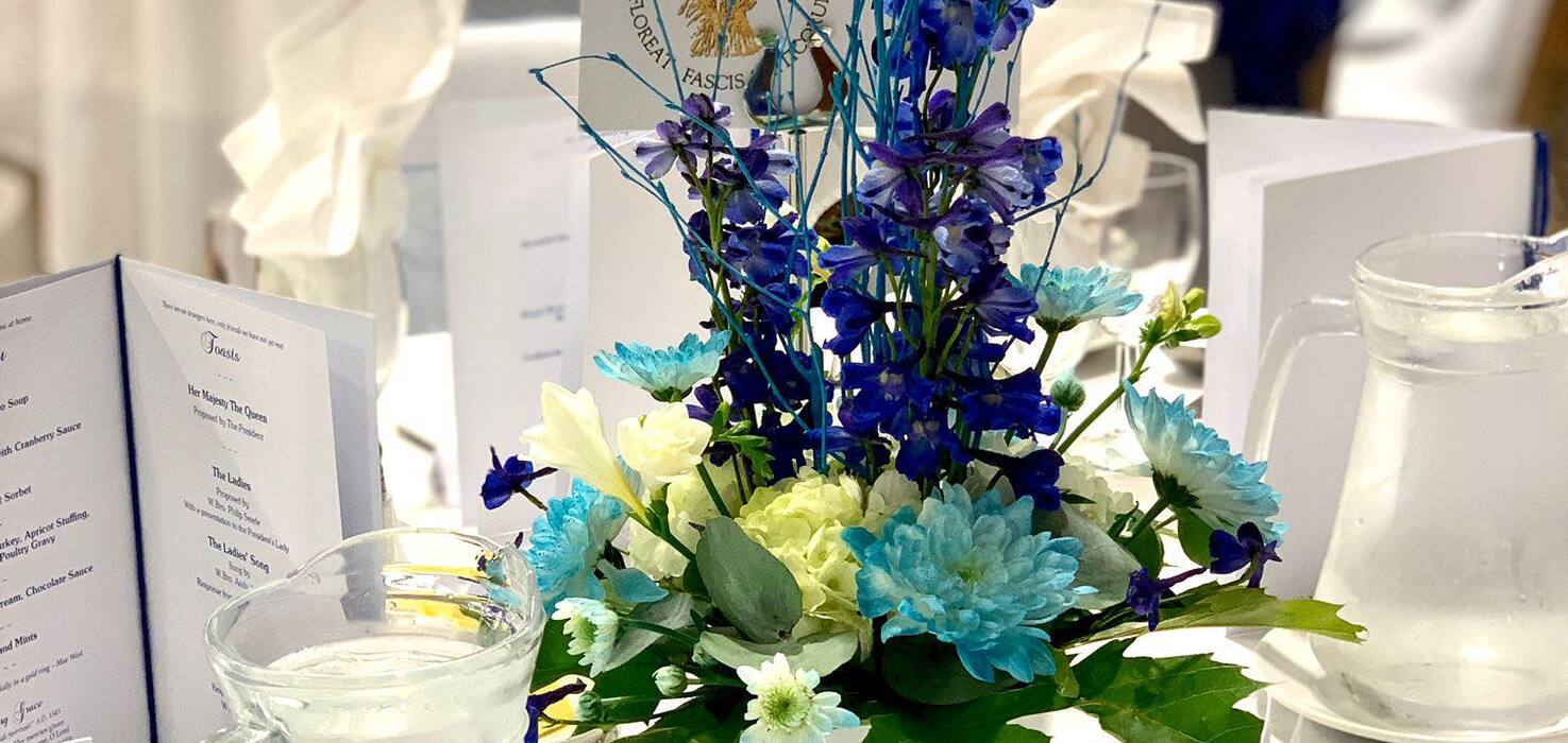 Blue and white floral centerpiece on mirrored plate at an elegant hotel banquet table with folded napkins, water pitchers and menu cards.