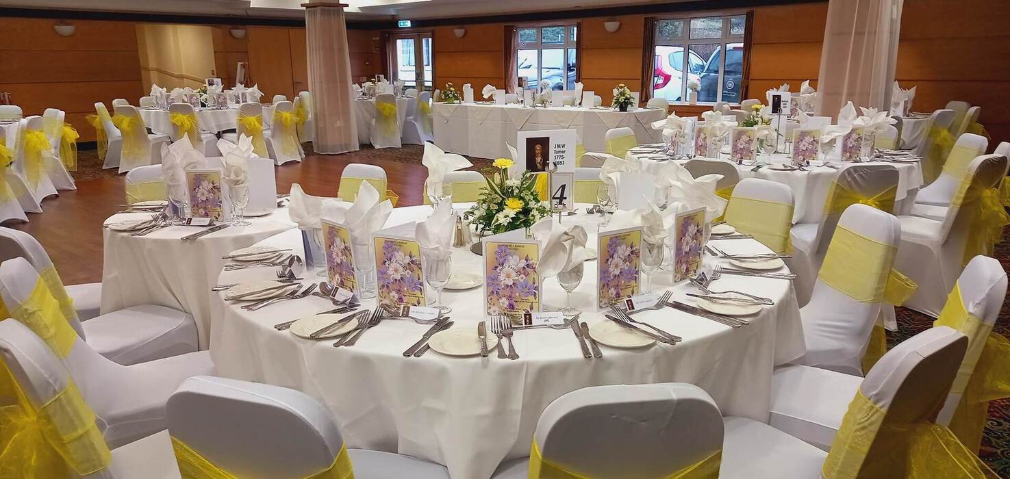 Hotel ballroom dressed for wedding with round tables, white linens, yellow chair sashes, floral centerpieces and dance floor