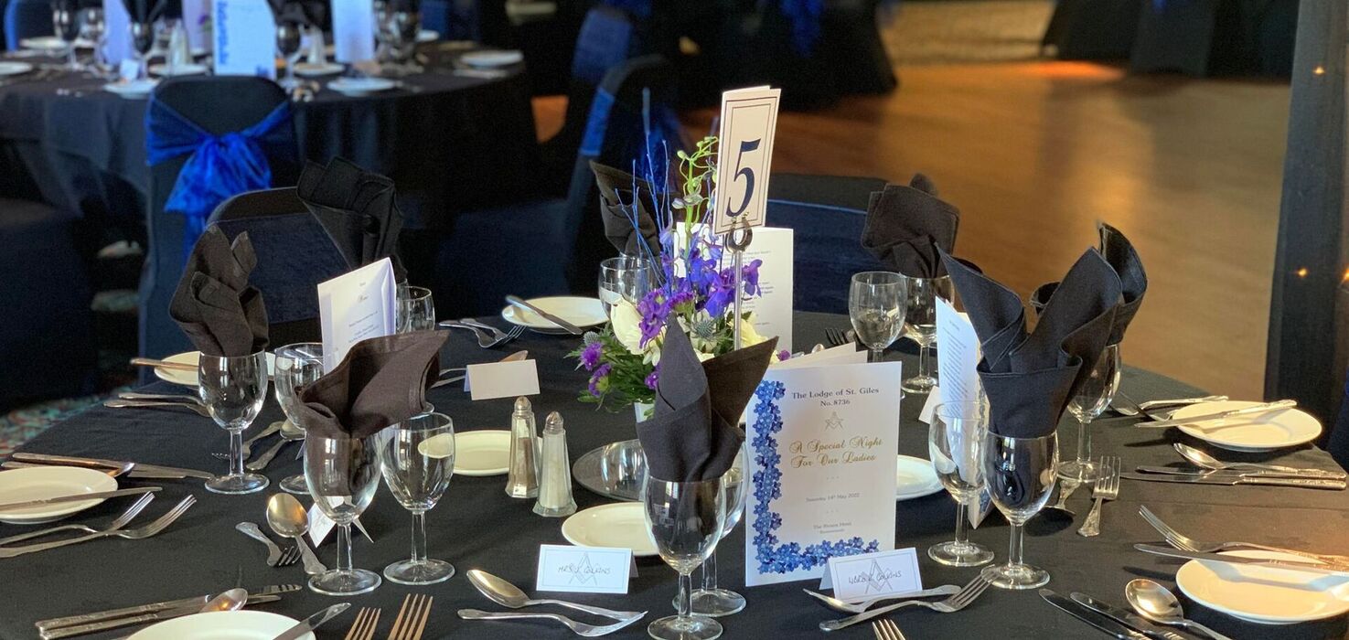 Formal banquet in a ballroom: round tables with black linens, royal-blue bows, folded black napkins and purple centerpieces.