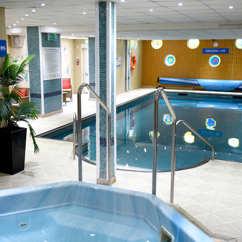Indoor hotel leisure pool and hot tub with tiled walls, handrails, pool cover, seating area and lifebuoy.