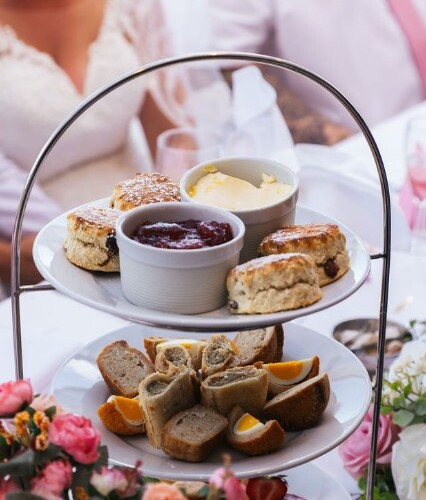 Three-tier tea stand with scones, jam, clotted cream, finger sandwiches and pastries on a floral wedding reception table.