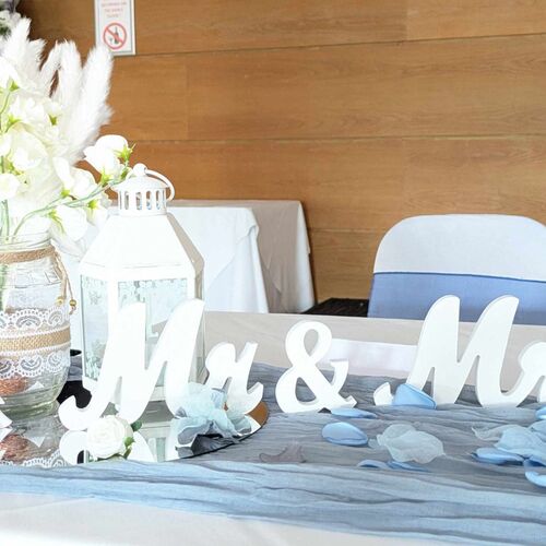 Wedding head table with white 'Mr & Mrs' sign, lace-wrapped mason jar of white flowers, white lantern and blue petal accents.