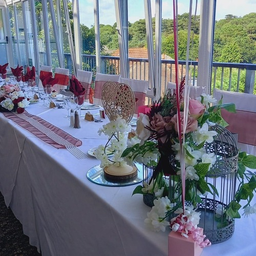 Banquet table with white linens, pink sashes, folded napkins, floral centerpieces and floor-to-ceiling windows over trees