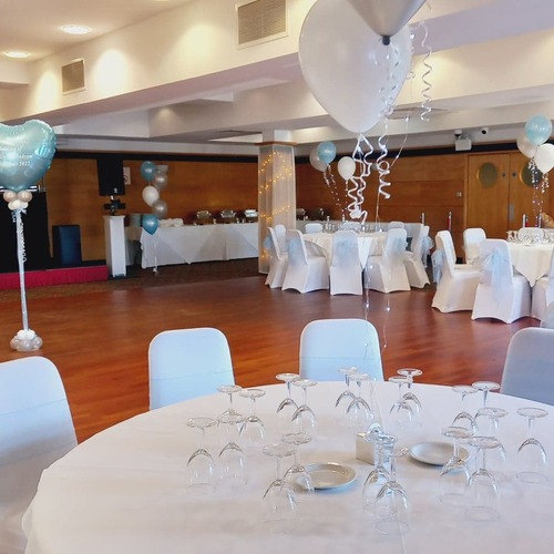 Banquet hall set for a wedding: round tables with white covers, pale blue bows, balloons, dance floor and DJ stage.