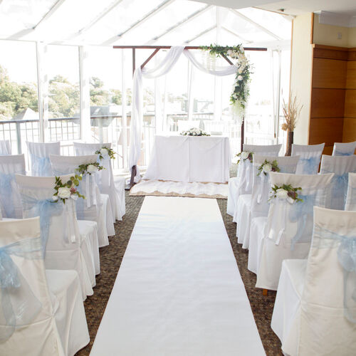 Sunlit conservatory wedding: white aisle, chairs with pale-blue bows, floral wooden arch and signing table