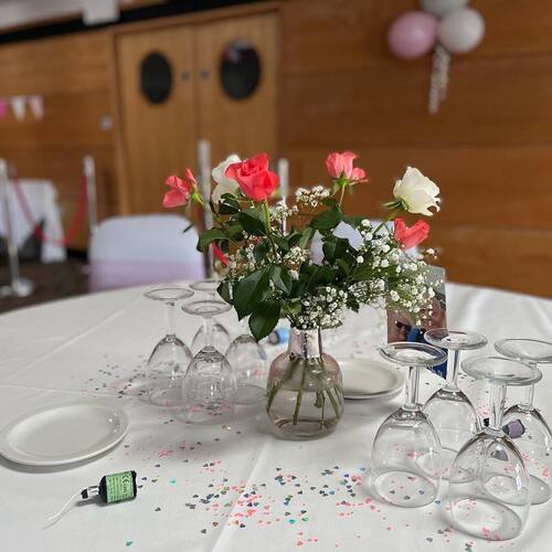 Round table with pink and white rose centerpiece, baby's breath, heart confetti and upside-down wine glasses at reception