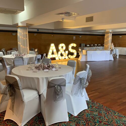 Wedding reception: round tables with white covers and grey sashes, lit marquee A&S, fairy-lit pillars, buffet, dance floor.