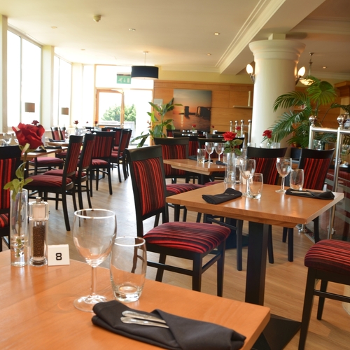 Sunlit hotel restaurant with wooden tables, red-striped chairs, single red roses and neatly set glassware